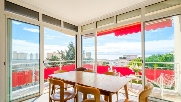A balcony with a table and chairs, large windows, and a red awning. - Bright 1-Bedroom Apartment with Sea View, 10 Minutes from the Beach (Cagnes sur Mer)
