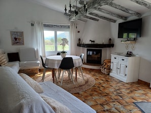 A cozy room with a fireplace, a dining table with chairs, a sofa, and a television mounted on the wall.
