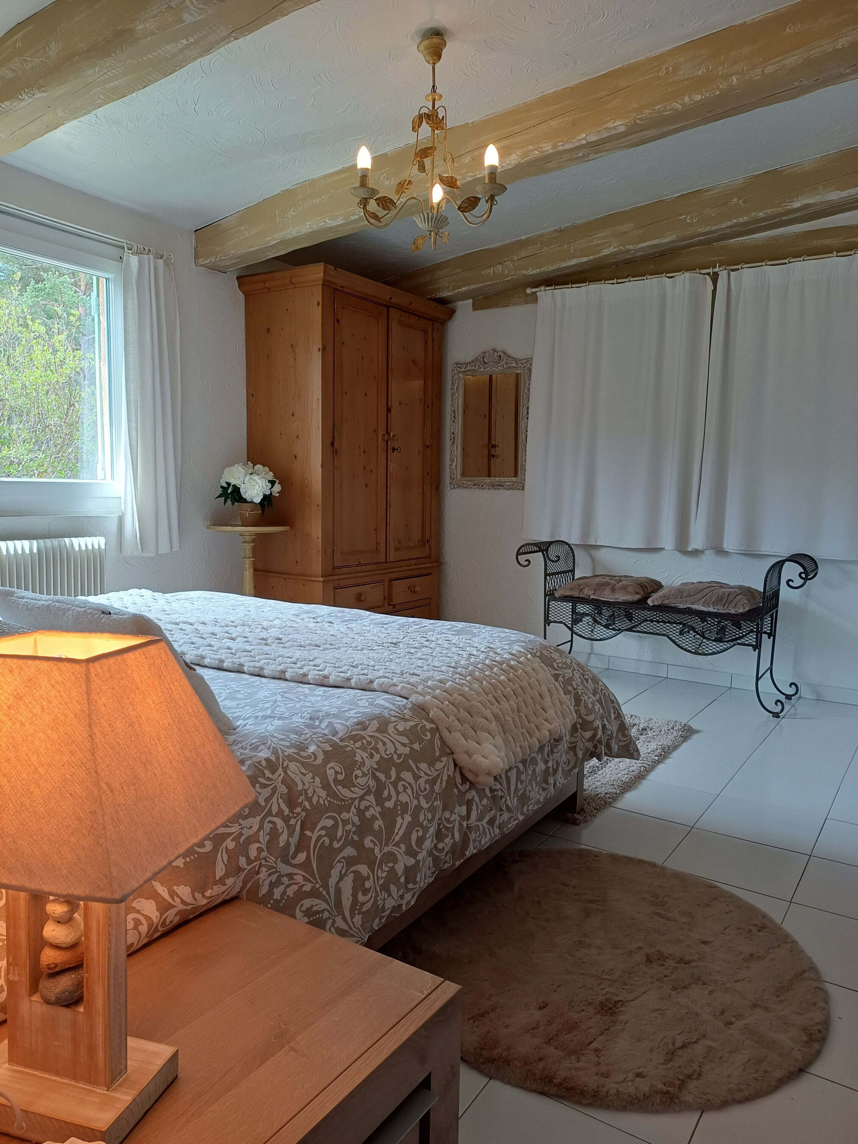 Un dormitorio con dos camas, un armario de madera, una araña, una mesita de noche con una lámpara y una ventana con cortinas.