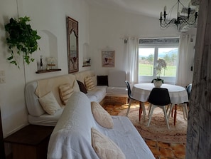 A cozy living room with a white sofa, a dining table, and a view of the outdoors.