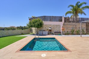 A rectangular swimming pool with a checkered tile pattern, surrounded by a patio with beige tiles.