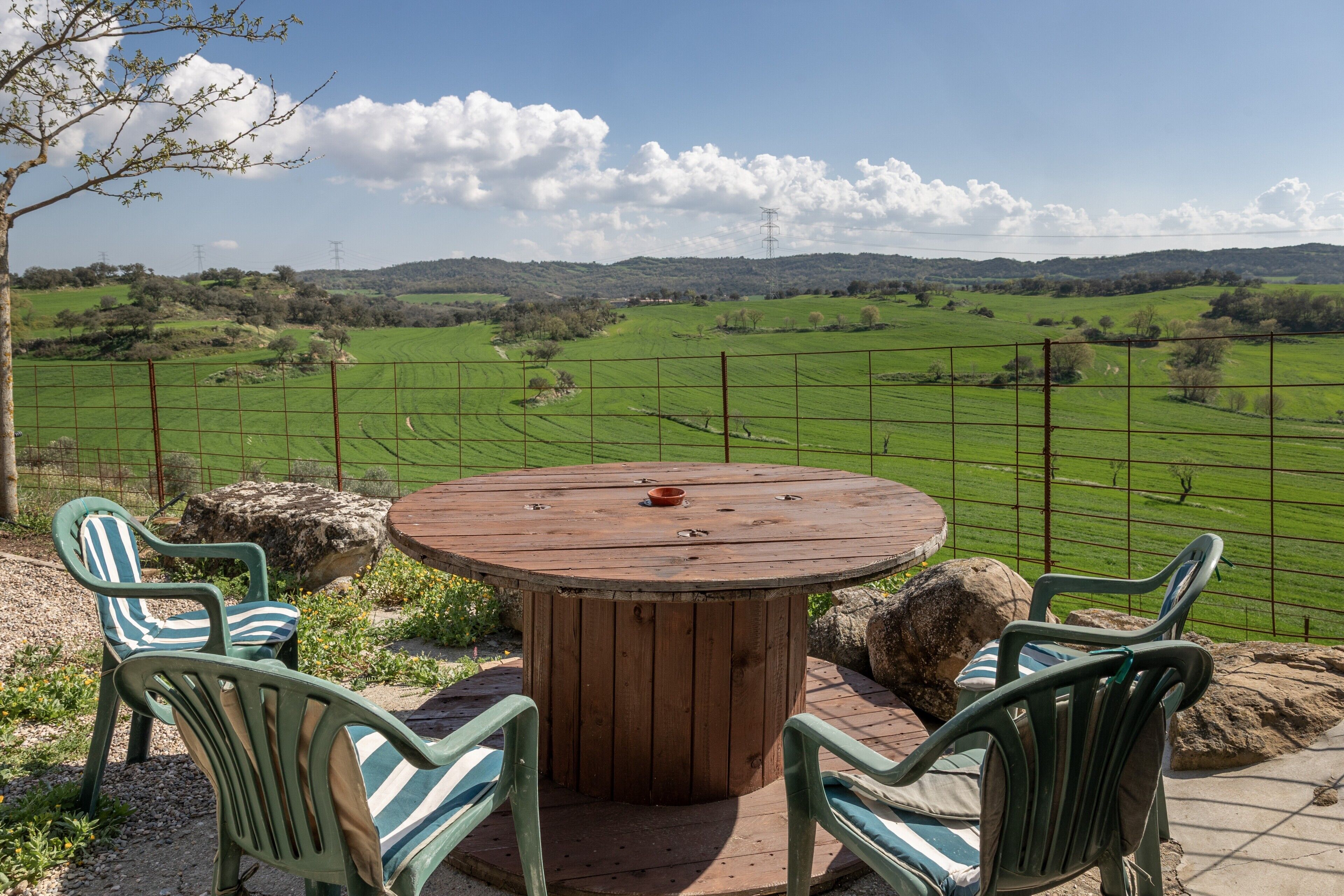 Une table ronde en bois, entourée de chaises, avec vue sur un champ verdoyant et une clôture.