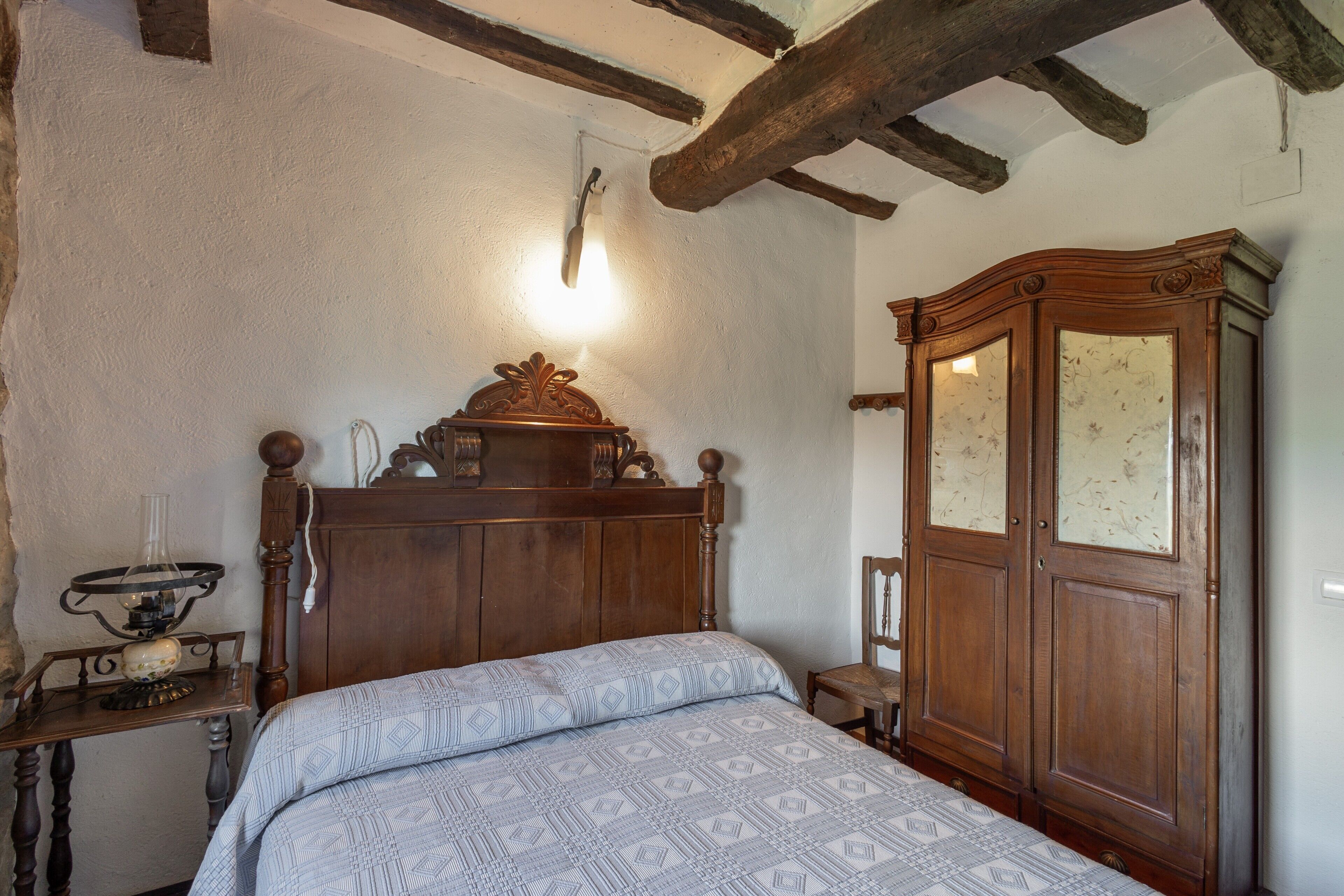 A bedroom with a wooden bed, a wooden wardrobe, and a wall-mounted light fixture.
