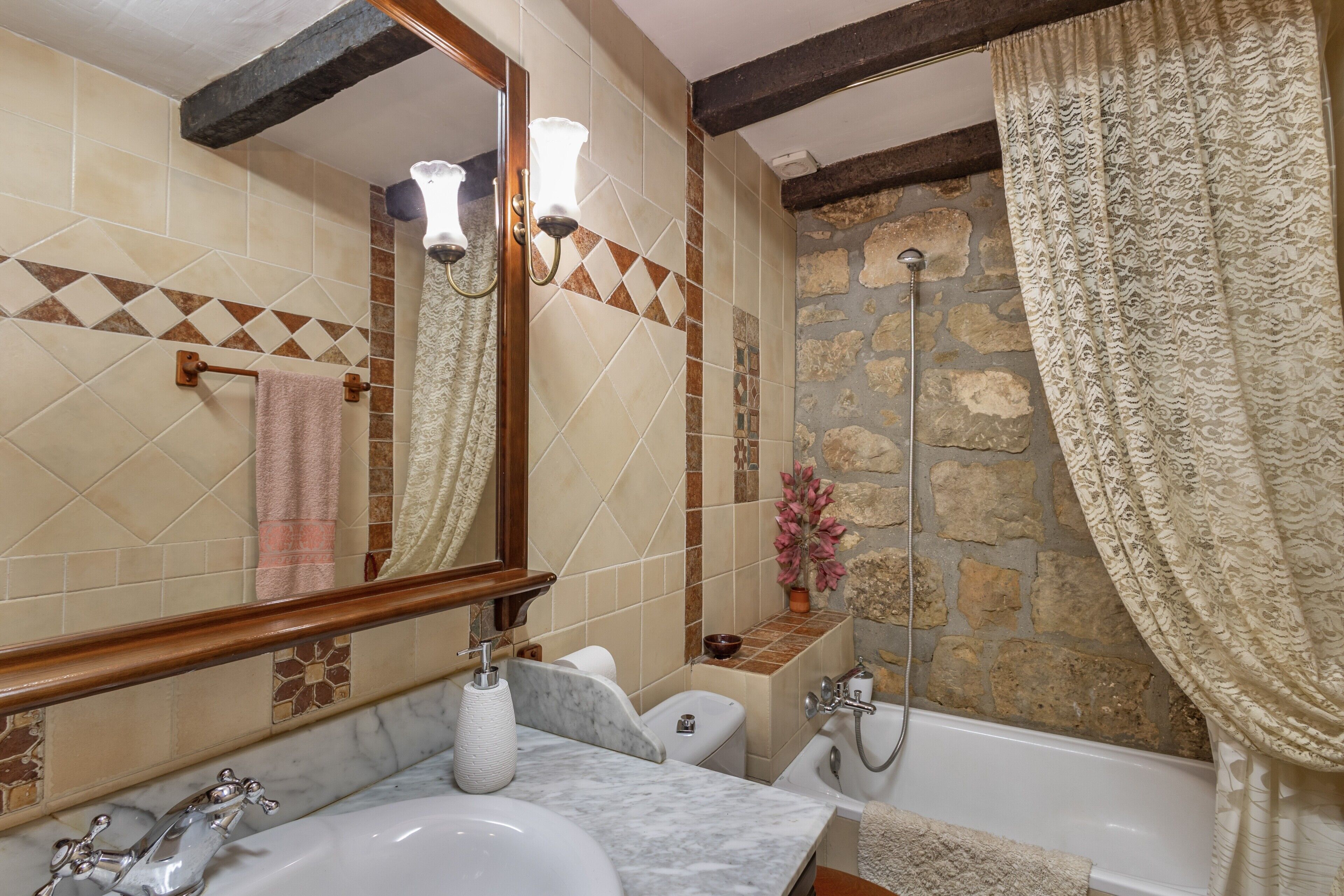 A bathroom with a marble sink, a bathtub, a stone wall, and a mirror with a towel rack.