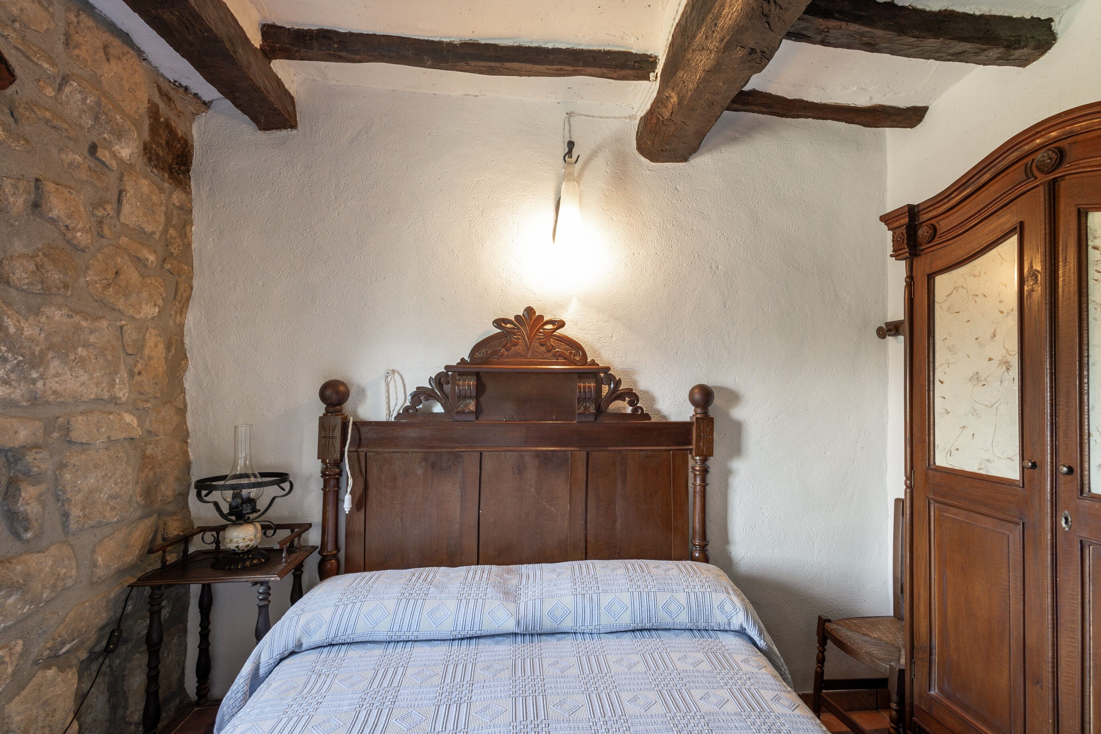 Een slaapkamer met een houten bed, een nachtkastje, een lamp en een kledingkast.