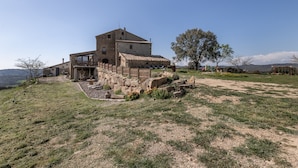 A rustic stone building with a balcony, surrounded by a grassy area and a large tree. - Country House 'Masia Manonelles' with Private Pool, Terrace & Air Conditioning (Unknown)