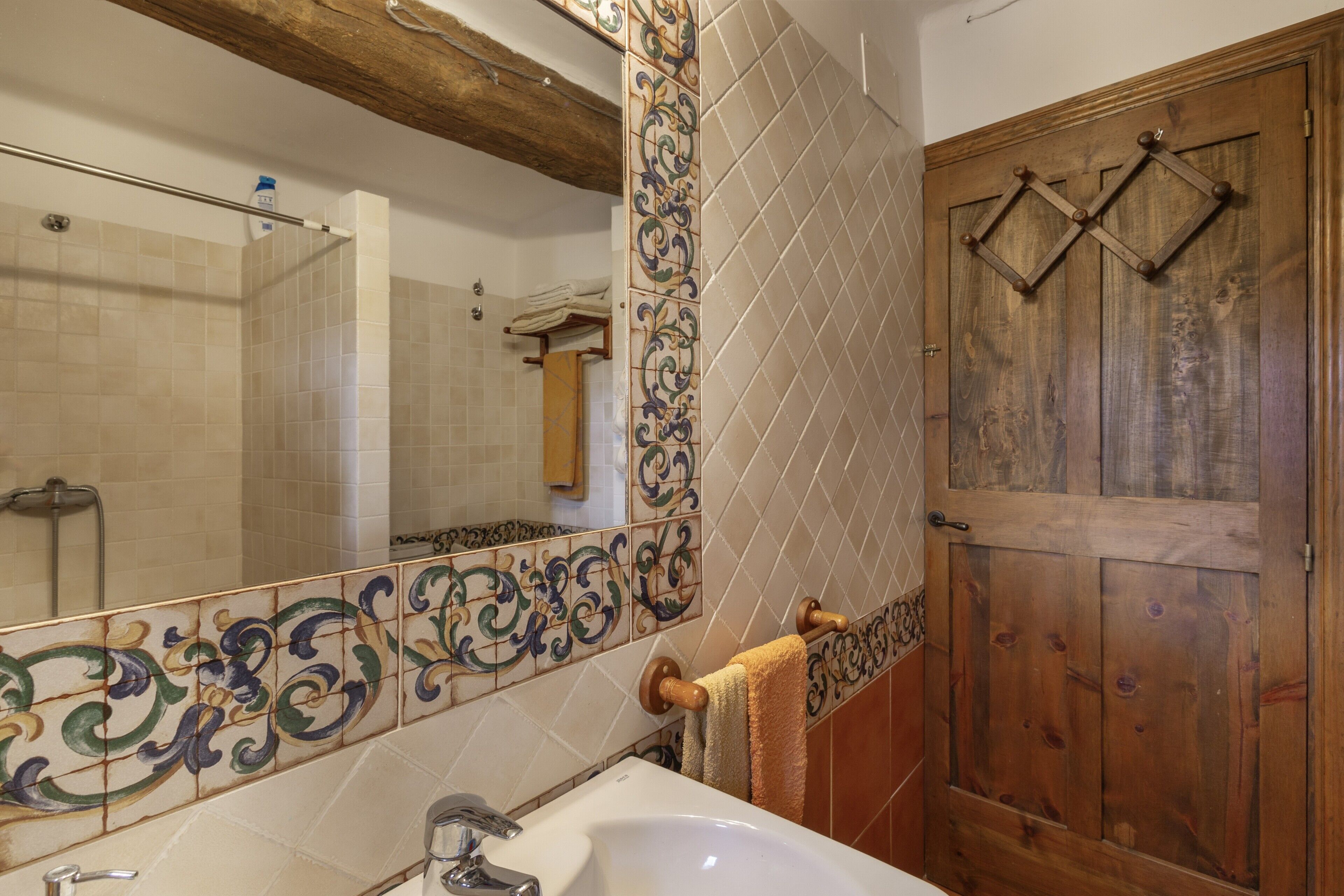 A bathroom with a sink, mirror, wooden door, and tiled walls.