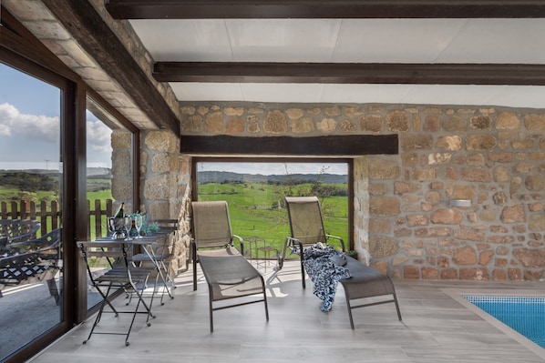 A room with a stone wall, a pool, and a view of the countryside.