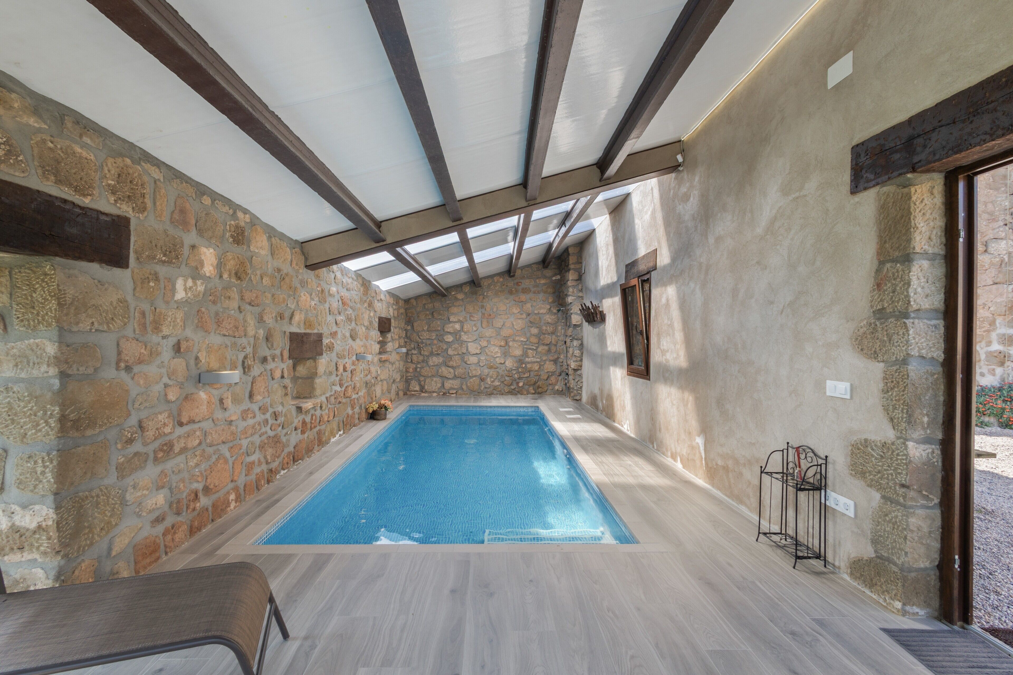 An indoor swimming pool with stone walls and a wooden floor, a bench, and a metal rack.