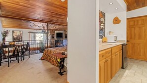 A room with a wooden ceiling, a fireplace, a dining area with chairs and a table, and a kitchen with wooden cabinets and a microwave. - Lovely Couples Suite with Amazing Views and Privacy (Emmett)