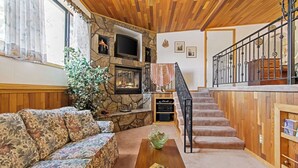 A cozy living room with a stone fireplace, a wooden staircase, and a sofa with floral cushions. - Lovely Couples Suite with Amazing Views and Privacy (Emmett)