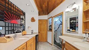 A modern bathroom with wooden cabinetry, a large mirror, and a decorative wall piece. - Lovely Couples Suite with Amazing Views and Privacy (Emmett)