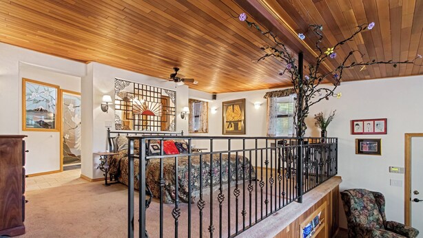A spacious living area with a wooden ceiling, a balcony with a wrought iron railing, and various artworks on the walls. - Lovely Couples Suite with Amazing Views and Privacy (Emmett)