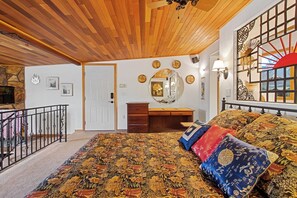 A bedroom with a wooden ceiling, a bed with patterned bedding, a desk, a mirror, and a decorative wall piece. - Lovely Couples Suite with Amazing Views and Privacy (Emmett)