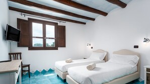 Un dormitorio con dos camas, un escritorio, una silla, un televisor y una ventana con contraventanas de madera.