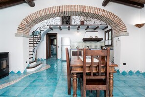 A dining area with a wooden table and chairs, a kitchen in the background, and a staircase leading to an upper level. - Holiday Home 'La Vela' with Sea View, Wi-Fi and Air Conditioning (Orosei)