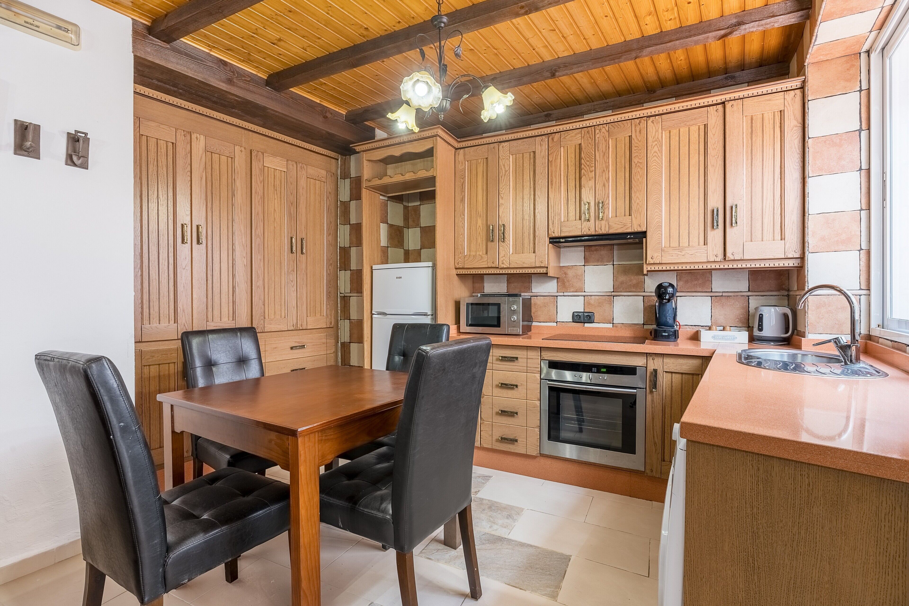 Una cocina con armarios de madera, una mesa de comedor con sillas, un microondas, una cafetera y un fregadero.