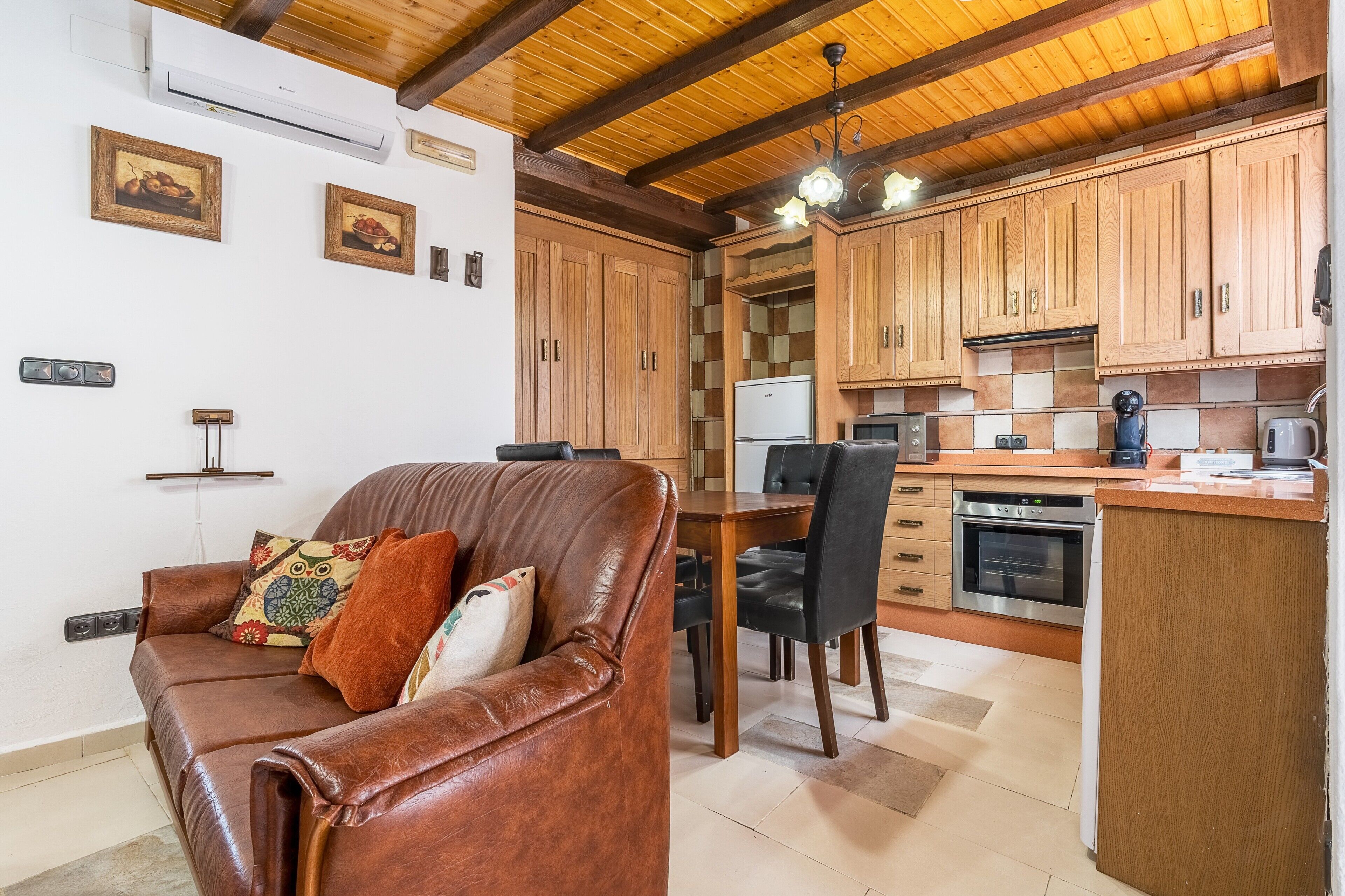 Una cocina con armarios de madera, una mesa de comedor y un sofá con cojín.