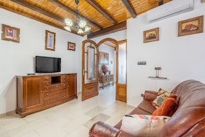 A living room with a wooden ceiling, a television on a cabinet, a brown leather sofa, and a door leading to another room.