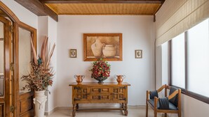 A wooden console table with a vase of flowers, a painting above it, and a chair by a window. - Holiday Apartment 'Planta Baja' (Íllora)