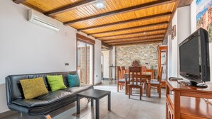 Ein Wohnzimmer mit einer schwarzen Ledersofa, einem Holzesstisch mit Stühlen, einem Fernseher auf einem Holzboden und einer Steinwand.