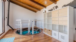 Ein Zimmer mit Holzboden, einem weißen Stauraum, einem runden weißen Tisch mit blauer Unterlage und einem Holzbalken an der Decke.