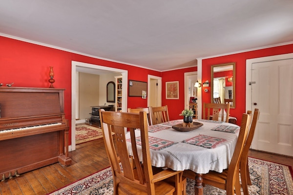 Dining room with wood table, chairs, piano, red walls, and wood floors.