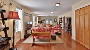 A spacious living room with a large floral sofa, wooden flooring, and a wooden wardrobe. - Chittenden Farmhouse: Historic 4BR/2BA, 20 Min to Killington, 7 Min to Mountaintop Resort (Chittenden)