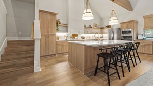 A spacious kitchen with wooden cabinets, a large island with bar stools, and modern appliances. - Charming new home in downtown New Braunfels, close to shops, dining & more! (New Braunfels)