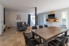 Un salon moderne comprenant un canapé, une table à manger, des chaises, un téléviseur et un mur d’accent en pierre.