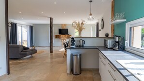 A modern kitchen with a central island, a dining area with a sofa, and a TV mounted on the wall. - Le Séchoir – Authentic House with Private Pool in Périgord Noir, Perfect for Families or Groups (Coly-Saint-Amand)