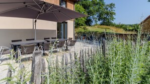 An outdoor patio with tables and chairs, a large umbrella, and a wooden fence. - Le Séchoir – Authentic House with Private Pool in Périgord Noir, Perfect for Families or Groups (Coly-Saint-Amand)
