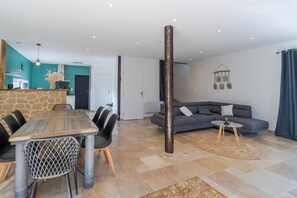 Un salon moderne avec une table en pierre, des chaises noires, un canapé gris et un pilier en bois.