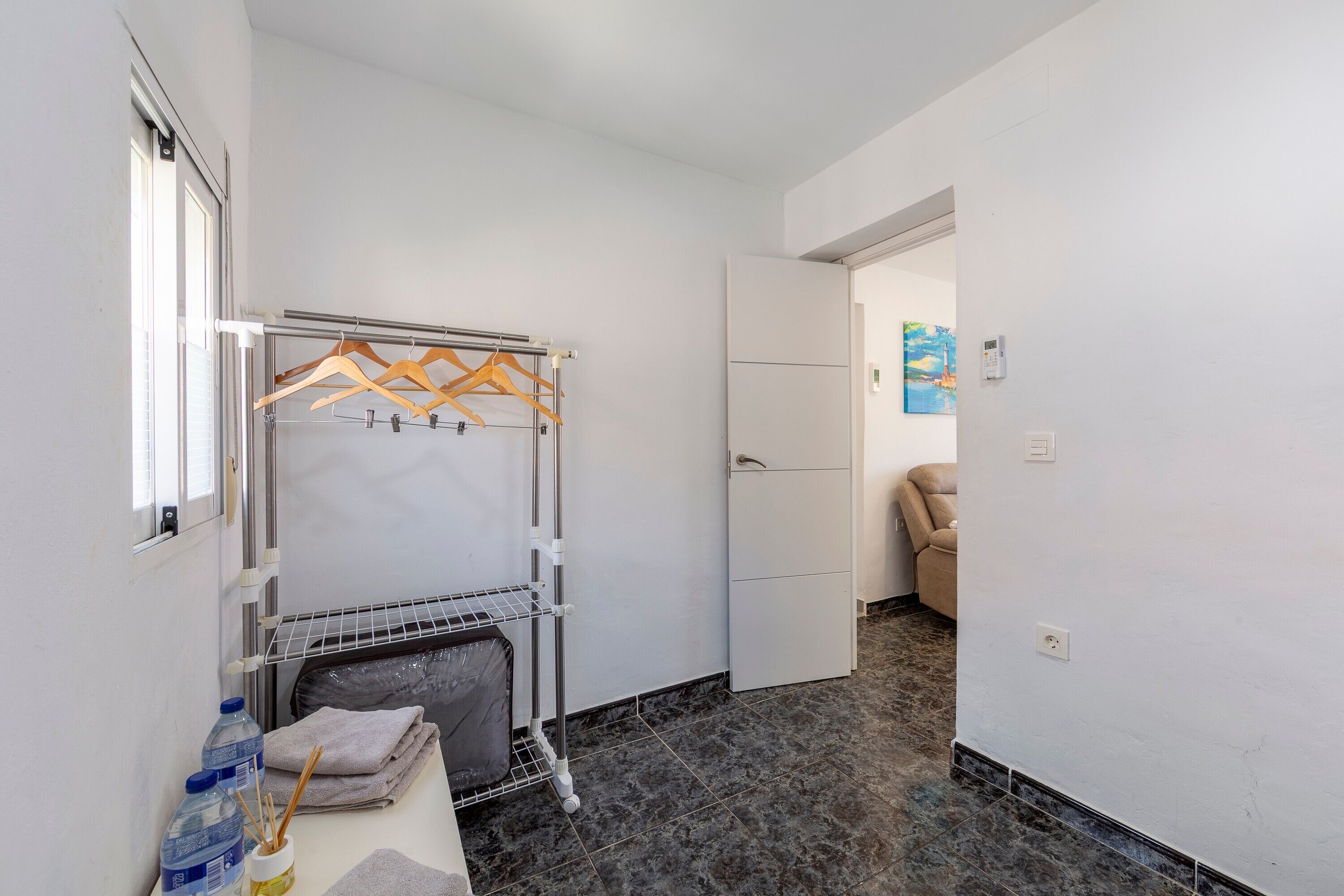 A hotel room with a bed, a drying rack, a radiator, a water dispenser, and a towel rack.
