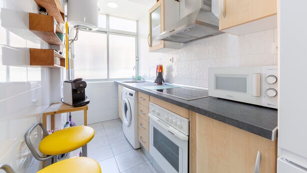 A modern kitchen with a washing machine, microwave, and wooden cabinets.