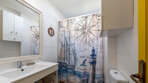 A bathroom with a nautical-themed shower curtain, a white sink, and a toilet.