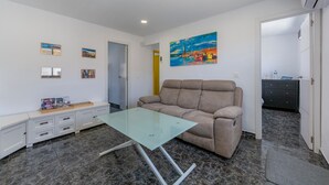 A room with a glass-top table, a beige sofa, a white cabinet, and a painting on the wall.