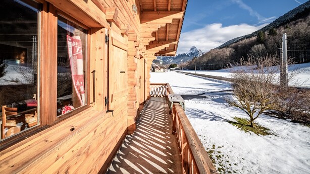 A wooden building with large windows, a wooden deck, and a snowy landscape with mountains in the background. - Chalet 'Phidel - 11 People' with Mountain Views, Private Terrace, and Wi-Fi (Bernex)