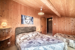 Habitación con paneles de madera, una cama, un cuadro colgado en la pared con un lobo, una lámpara colgante y una puerta que da a otra habitación.