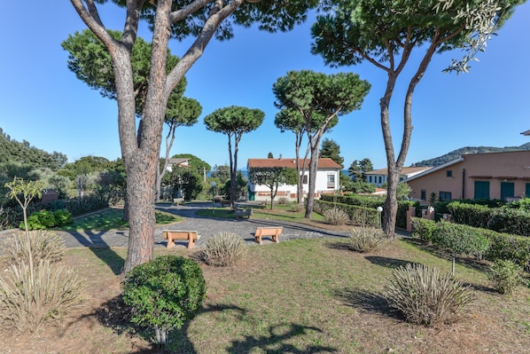 A landscaped garden with benches, trees, and a building with a red roof.