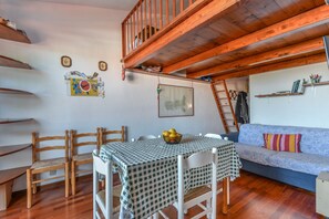 Een knus ingerichte kamer met een hoogslaper, een eettafel met stoelen, een bank en een ladder.