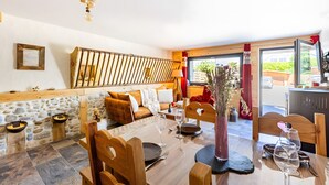 Une pièce chaleureuse avec un mur en pierre, des meubles en bois, une table à manger dressée pour deux personnes et une vue à travers une porte vitrée.