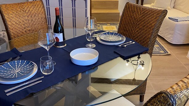 Une table à manger dressée avec des assiettes, des couverts et une bouteille de vin, entourée de chaises en osier dotées de coussins.