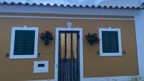 Un bâtiment à la façade marron, aux volets verts et à la porte centrale surmontée d’une enseigne.