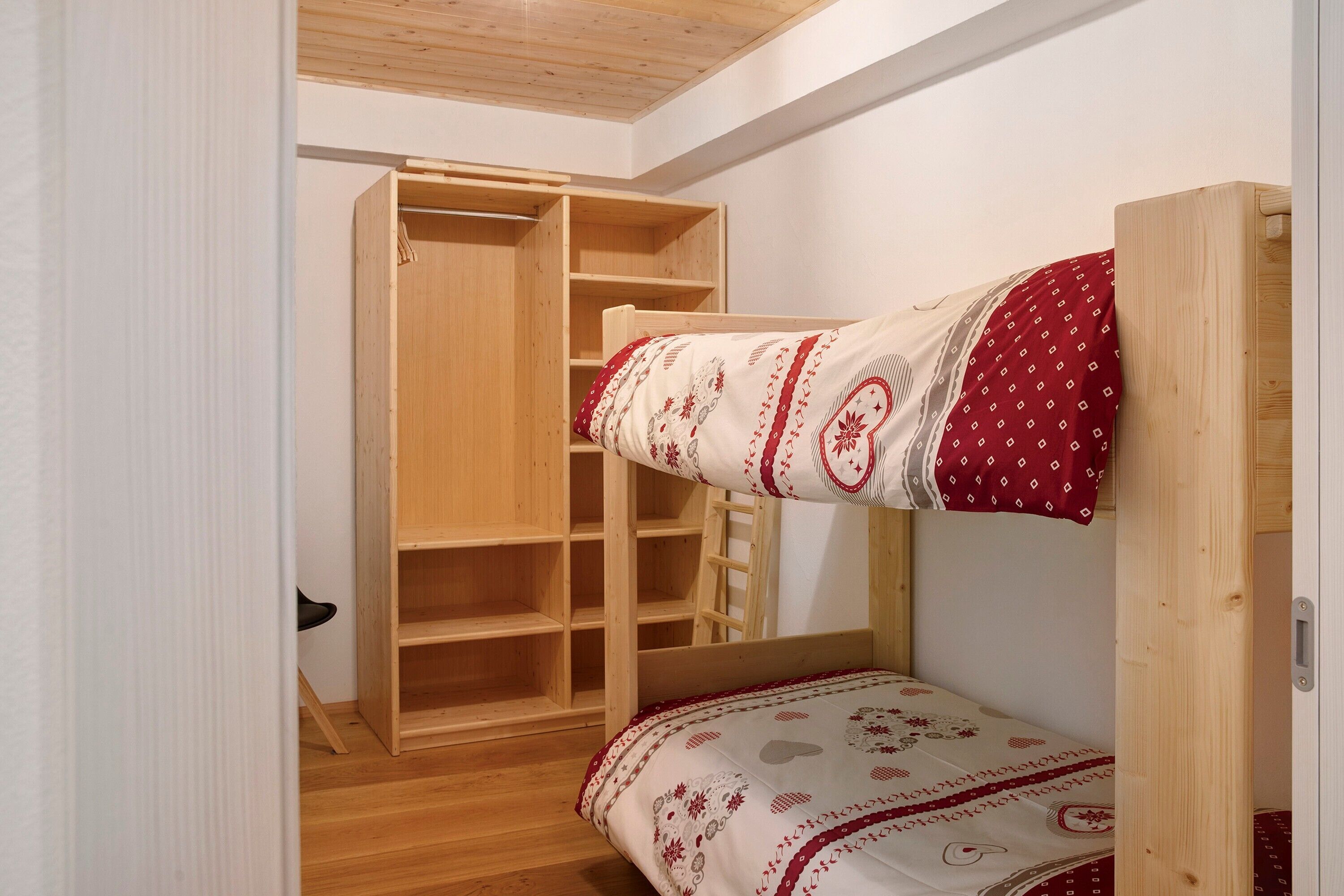 Ein Etagenbett mit gemustertem Bettbezug, ein Holzschrank mit vielen Regalen und eine Treppe.