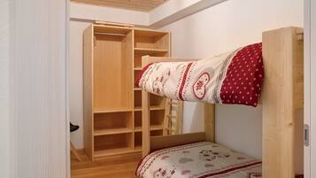 Ein Etagenbett mit gemustertem Bettbezug, ein Holzschrank mit vielen Regalen und eine Treppe.