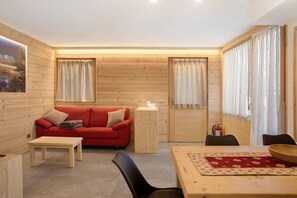 A log cabin interior with a red sofa, wooden tables, and curtains.