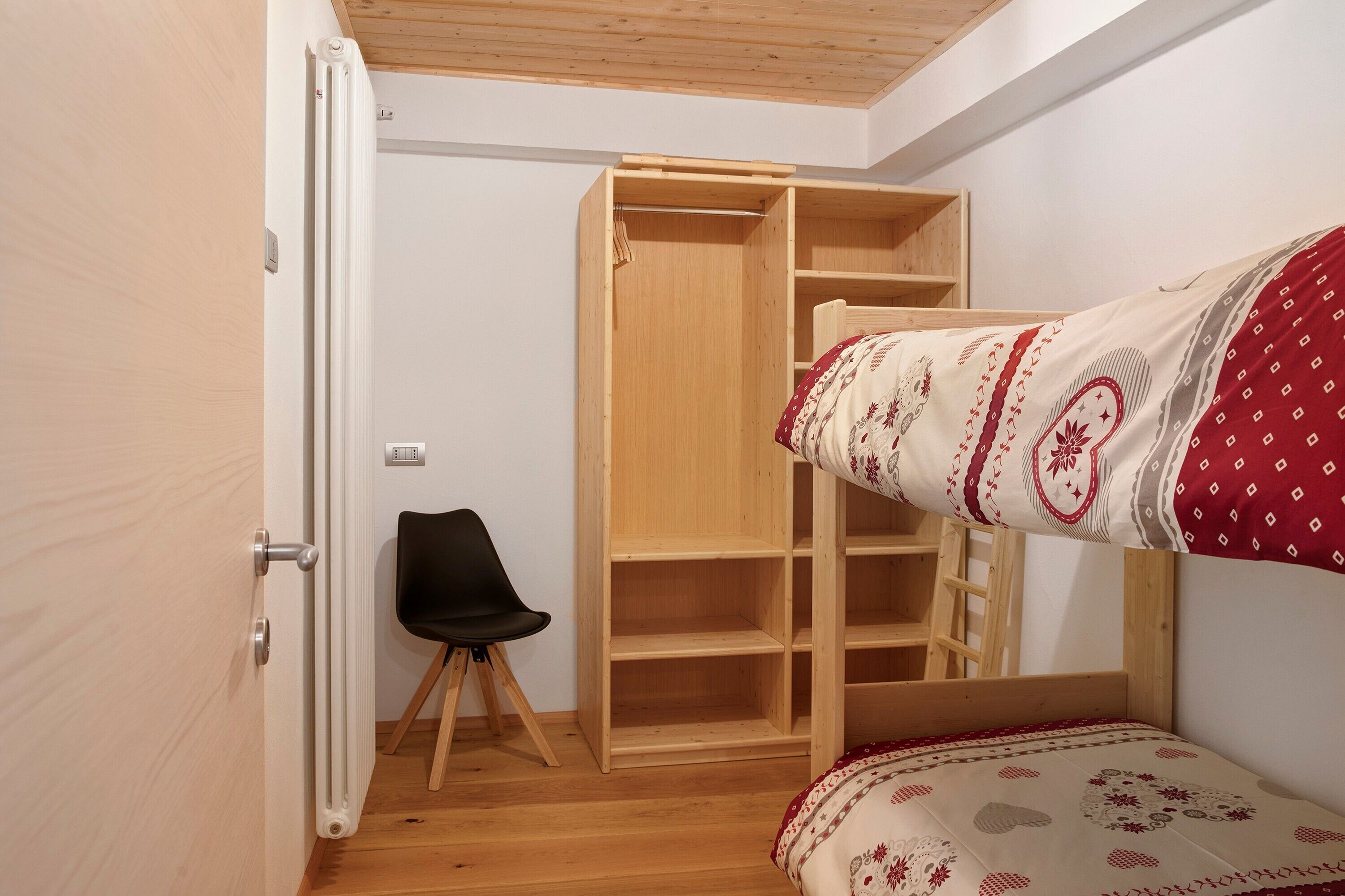 Une pièce avec un lit superposé, une armoire en bois, une chaise noire et une échelle en bois.