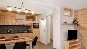 Una cocina moderna con armarios de madera, un comedor con sillas, un televisor sobre un mueble de madera y un pasillo con un espejo.