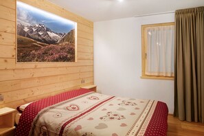 A wooden-paneled room with a bed, a window with curtains, and a wall-mounted picture of a mountain landscape.
